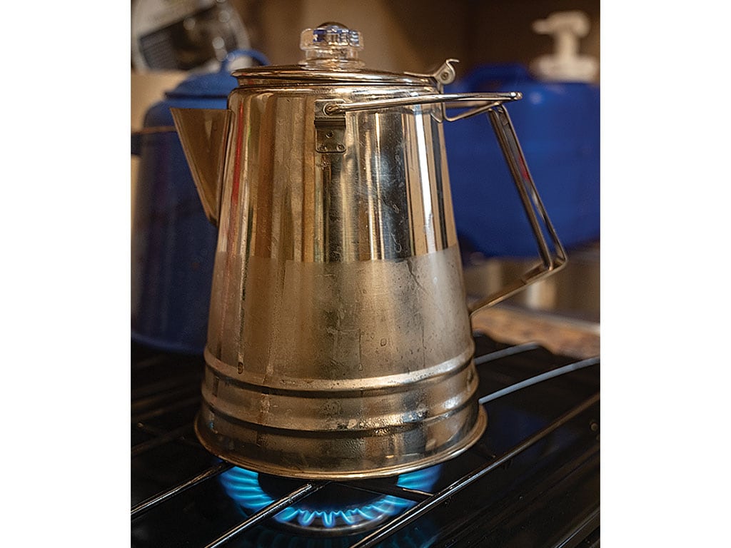 Stainless steel coffee pot on a gas stove with blue flame.