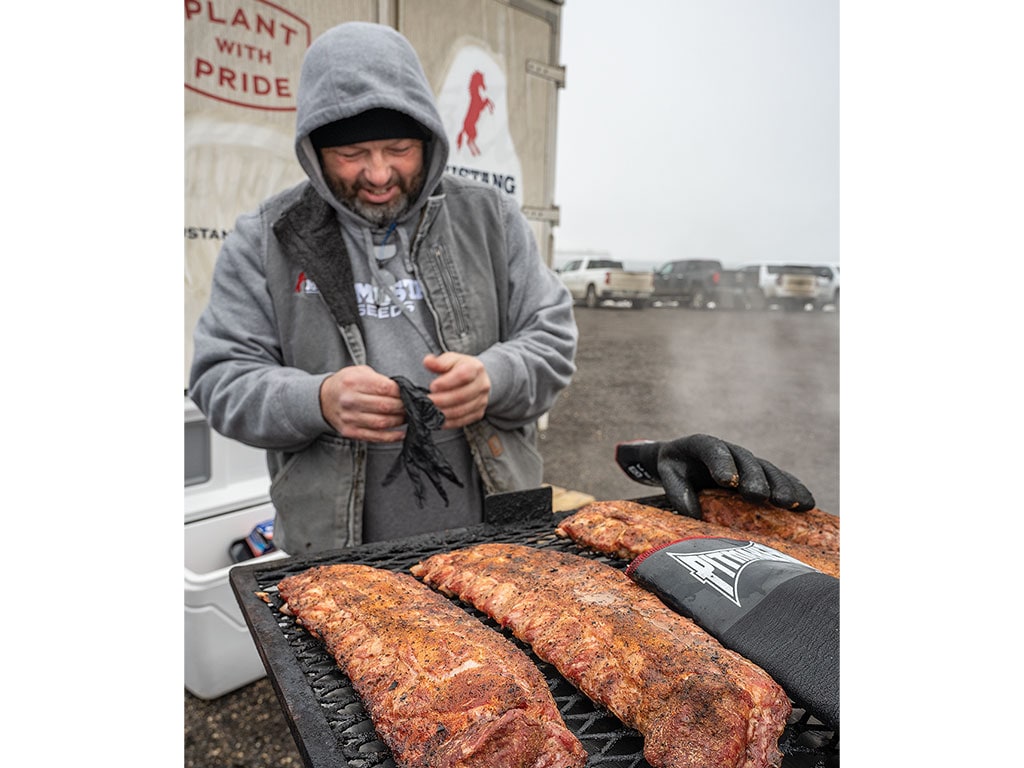 Person standing by a grill with seasoned barbecue ribs.