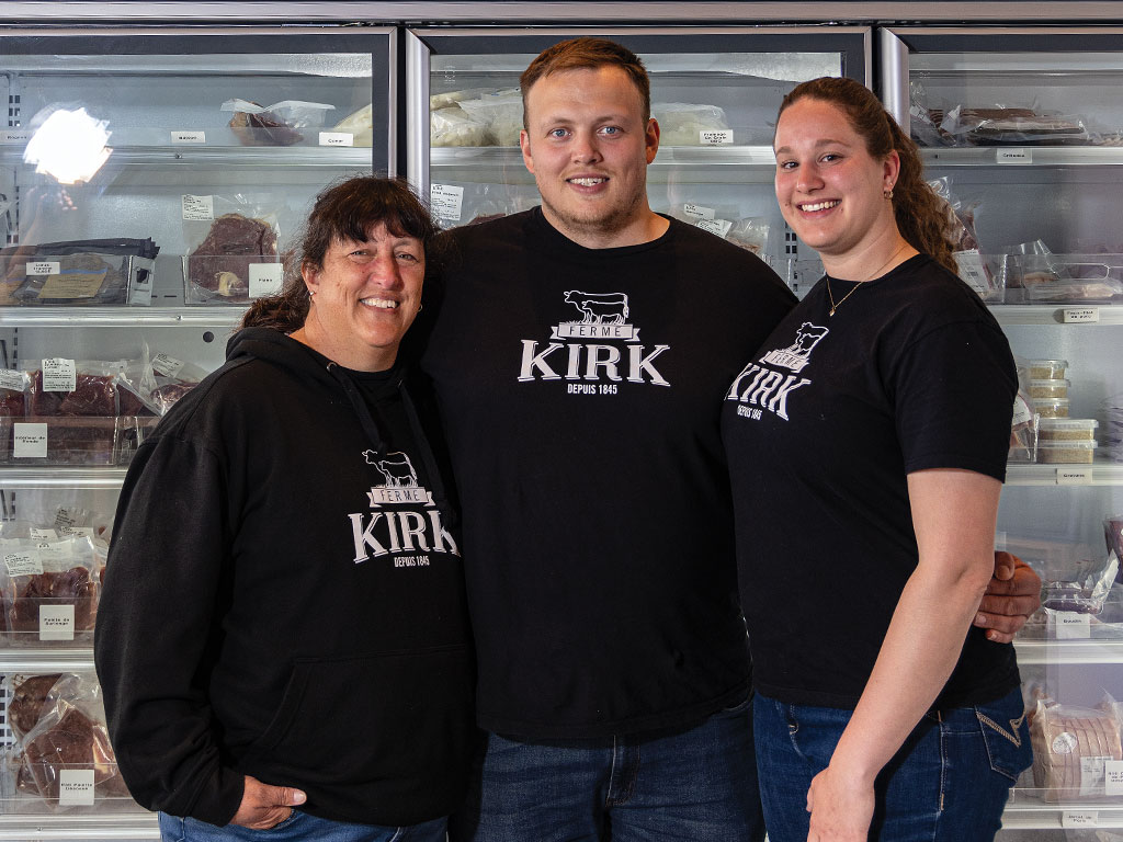 Three people in black shirts standing in front of a meat counter.