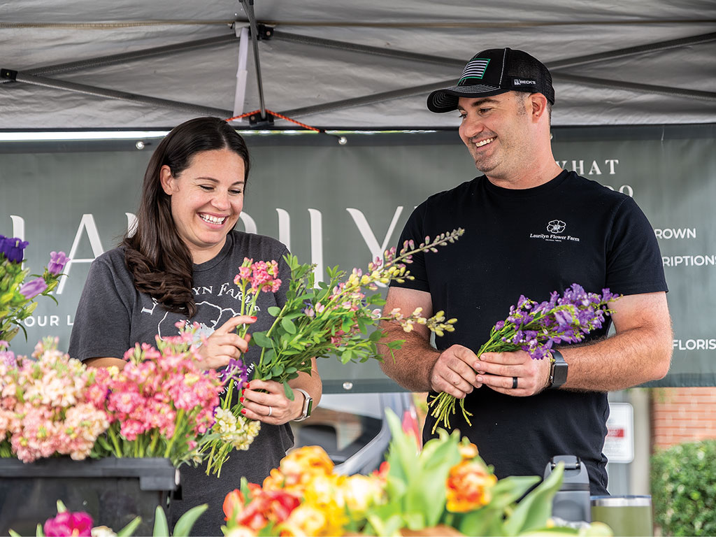 Two persons arranging flowers at a stall with various blooms on display.