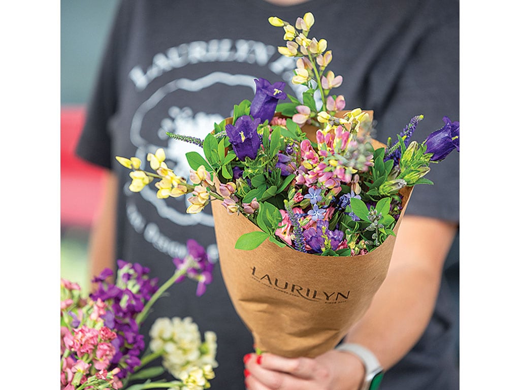 Person holding a bouquet of colorful flowers wrapped in brown paper.