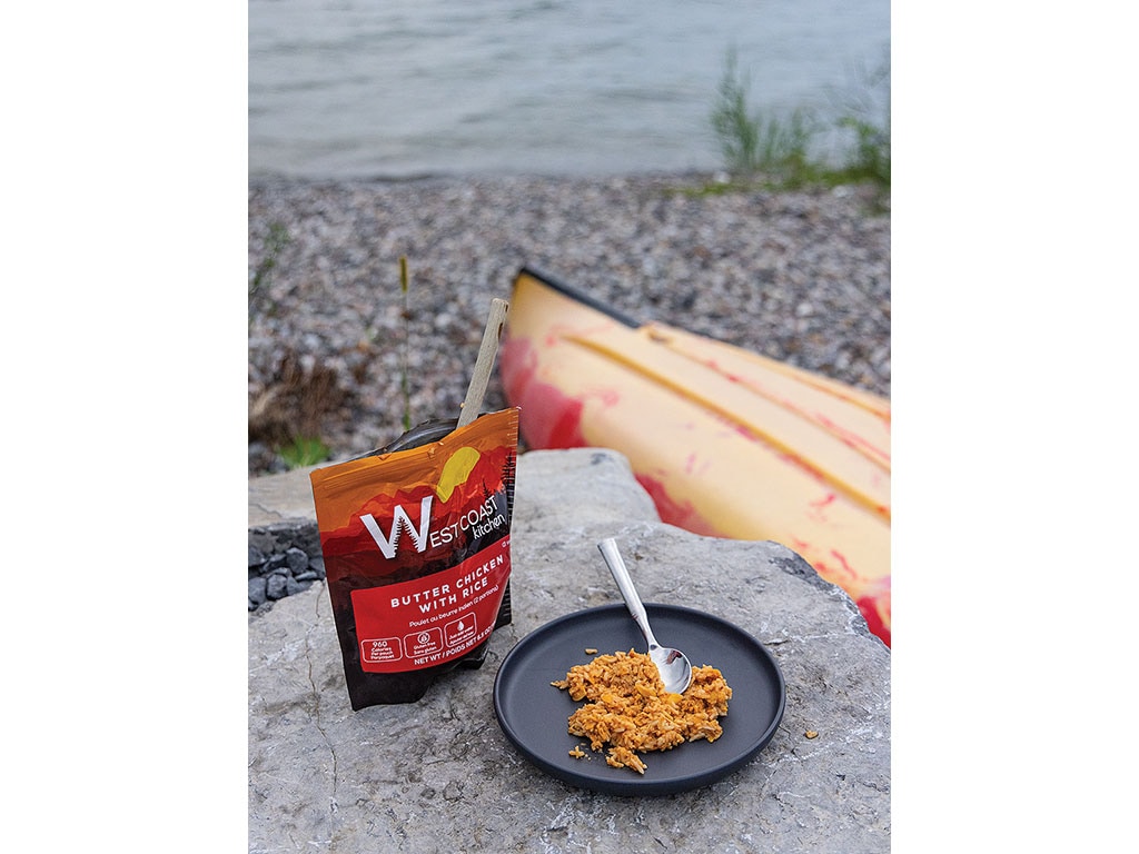 A meal of butter chicken with rice on a plate near a kayak.