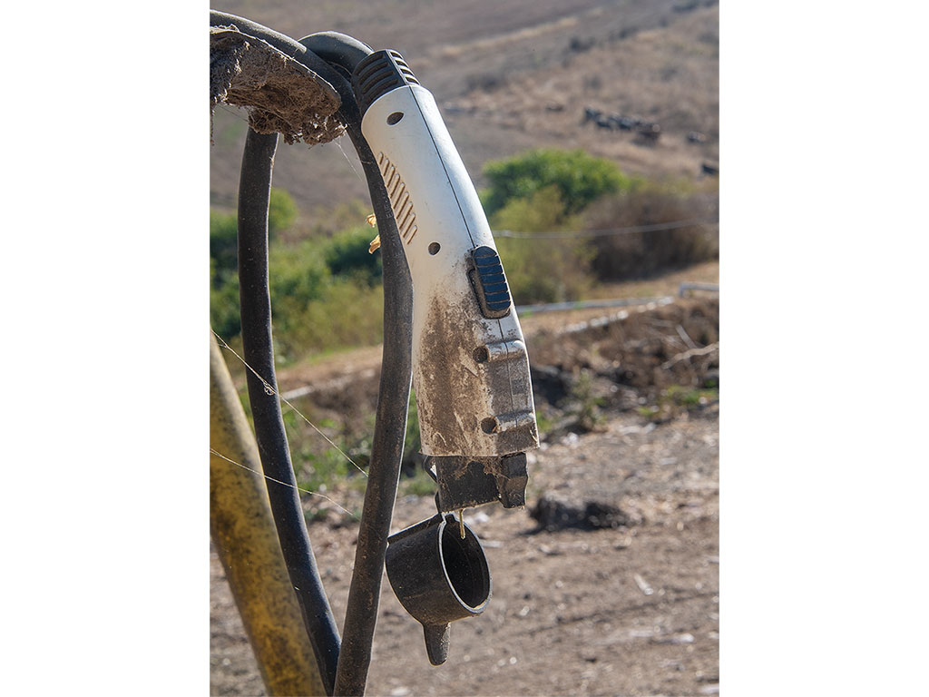 Close-up of a dirty electric charger against a rural backdrop.