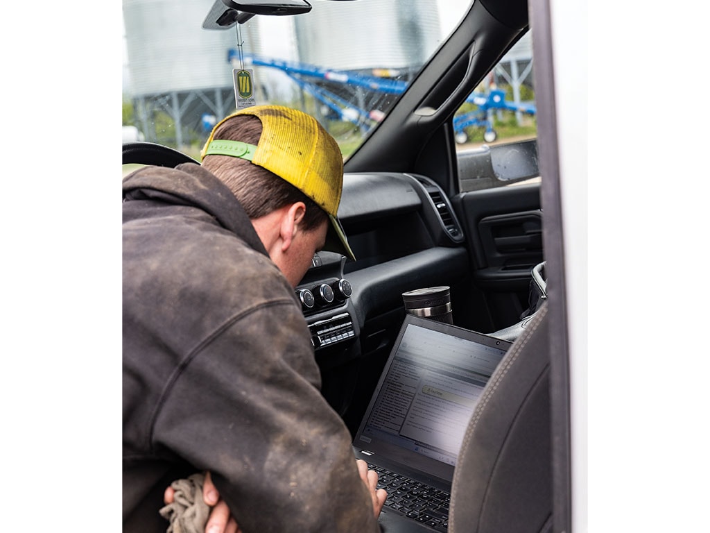 Person working on a laptop inside a vehicle with industrial equipment in the background.