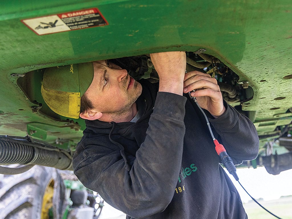 Person working on the underside of green agricultural machinery.