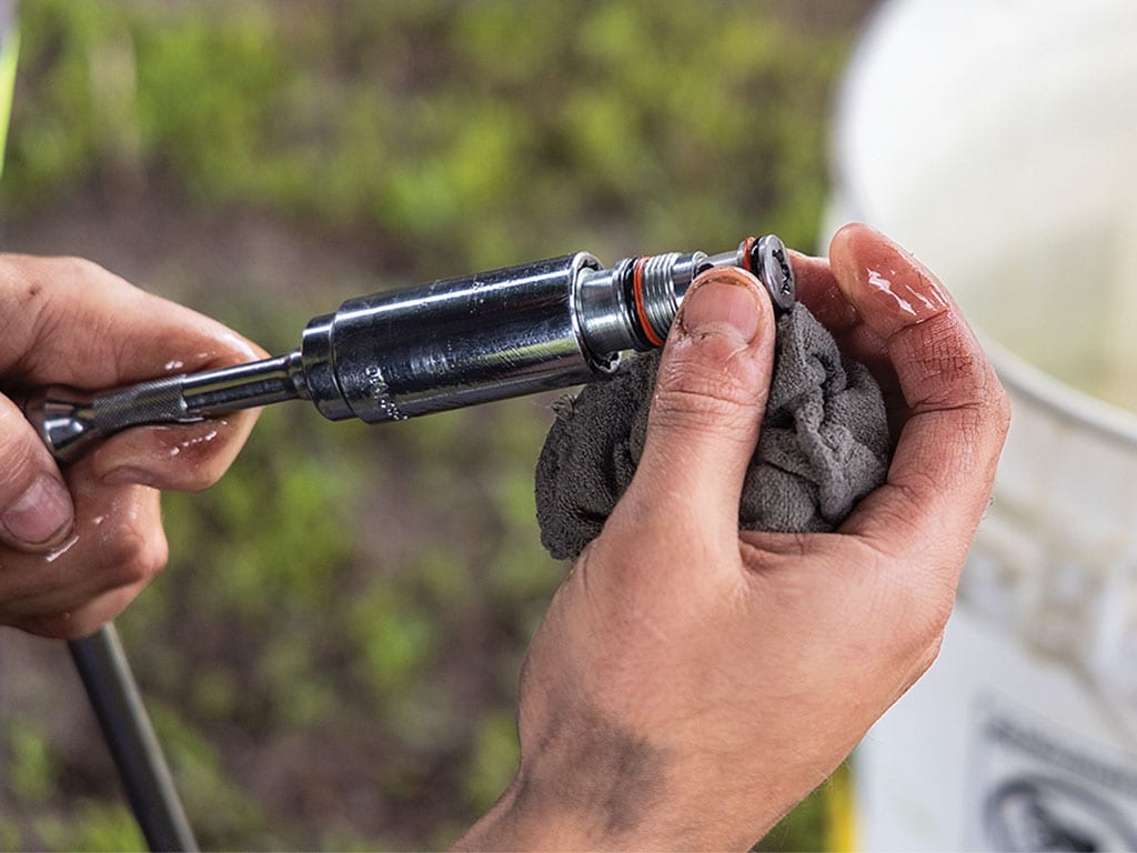 Hands cleaning a spark plug with a cloth and a tool outdoors.