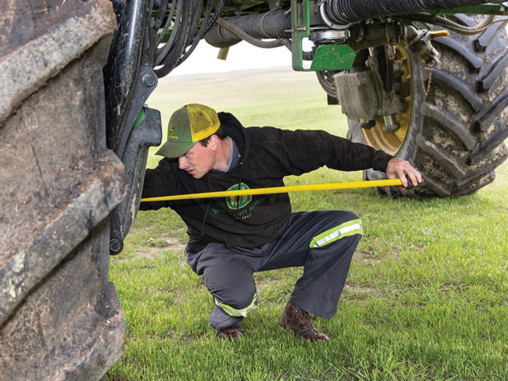 Person in workwear measuring under a tractor on grass.