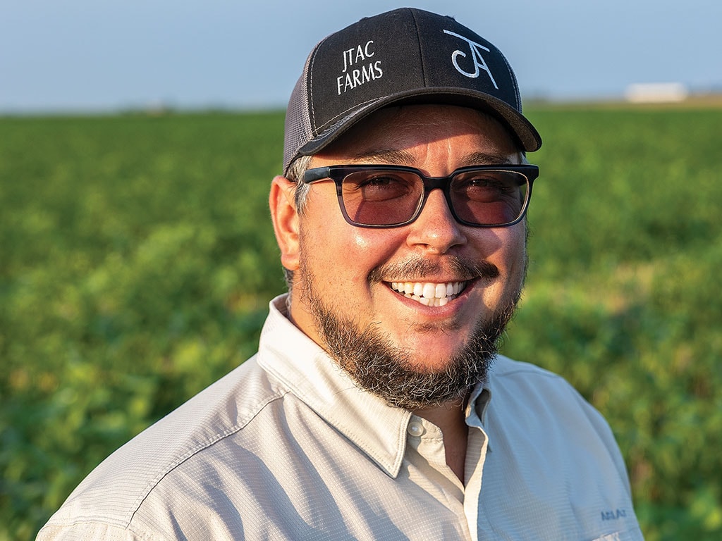 Person wearing a cap standing in front of a green field.