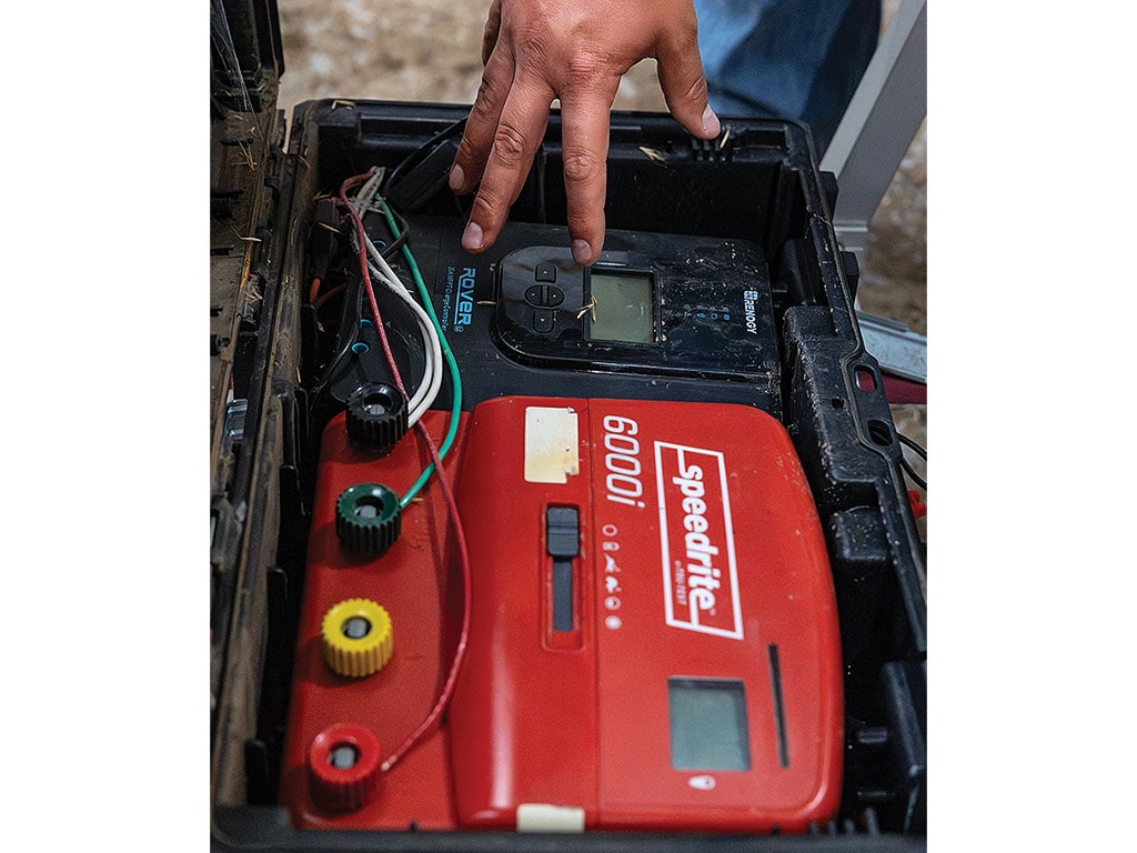 Hand adjusting equipment in an open electronic device case with cables and displays.