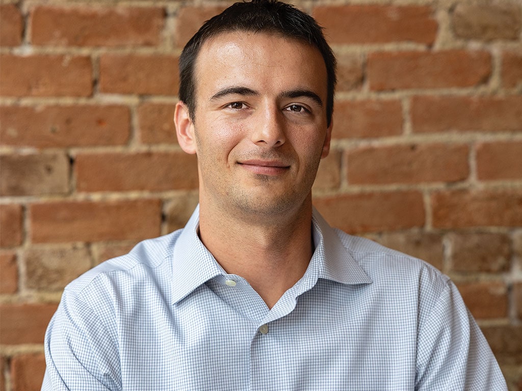 Person in a blue checkered shirt standing before a brick wall.