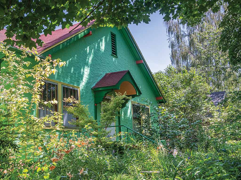 A bright green house surrounded by a variety of trees, bushes and shrubs