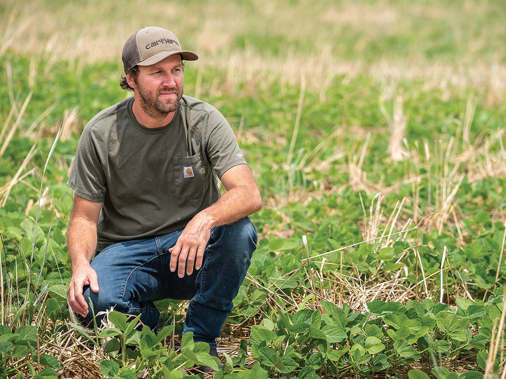 A farmer kneeling in a soybean field