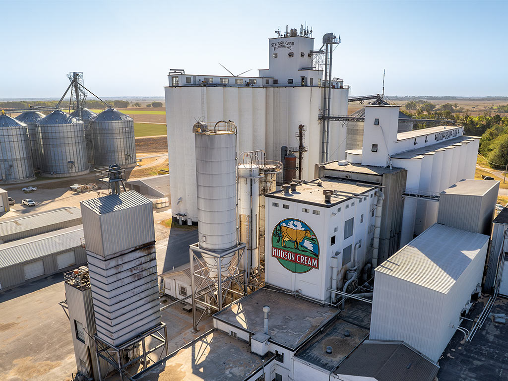 Aerial view of the Stafford County Flour Mill which consists of tall white buildings and steel silos from-field