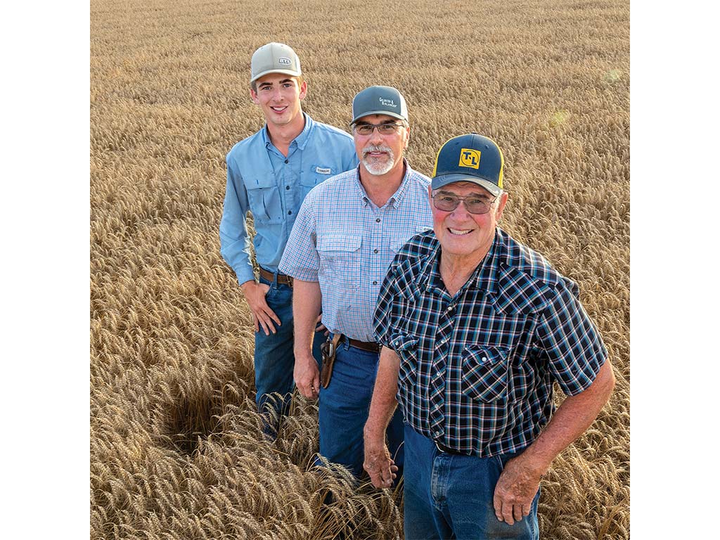 Three men in agricultural attire stand confidently in a vast wheat field, showcasing their connection to farming and harvest.