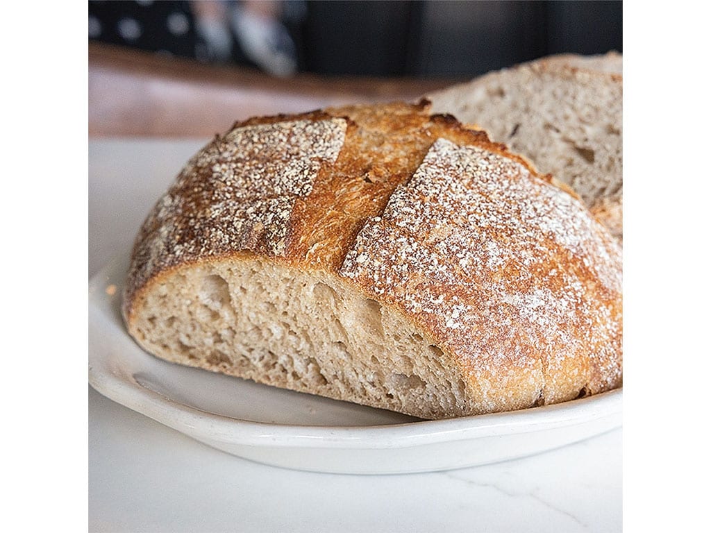 Close-up of a freshly baked loaf of artisan bread, showcasing a golden crust with flour dusting and a soft, airy interior.