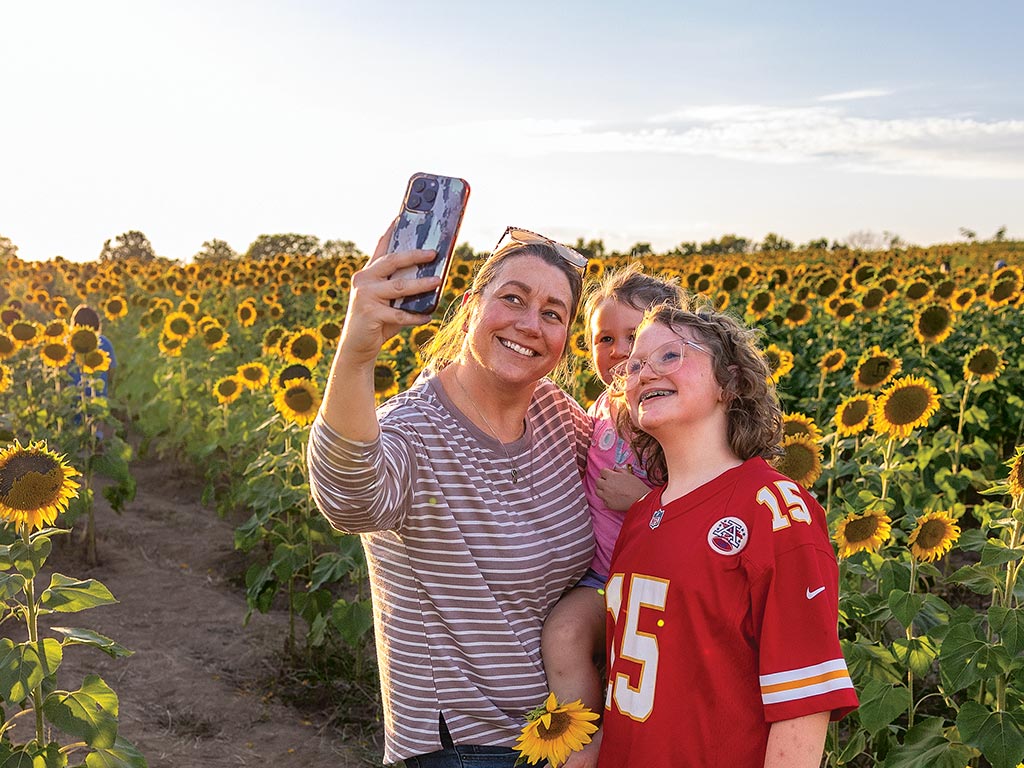 An adult and two children taking a selfie photo in front of a field of tall sunflowers