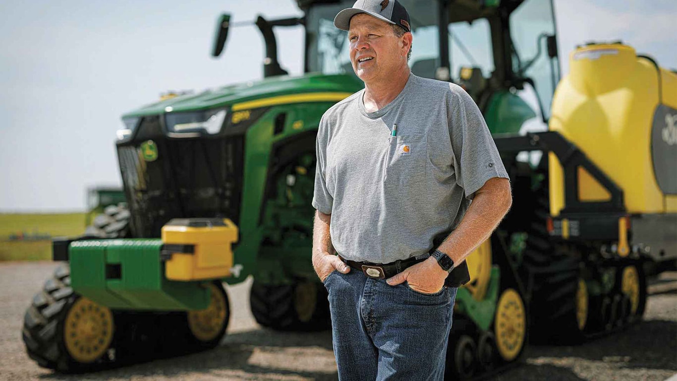 Person standing in front of a tractor and planter on a gravel lot.